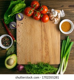 Wooden board with clear space. Around tomato and dill, olive oil, spice, peper, avocado, green onion, spinac and garlic. Top views. - Powered by Shutterstock
