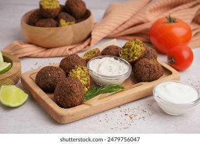 Wooden board with delicious falafel balls, lime, sauce and tomato on light background, closeup