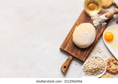 Wooden board with dough for preparing homemade cookies and ingredients on light background
