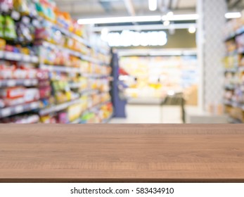 Wooden board empty table in front of of supermarket shelves. Perspective dark wood over blur in supermarket. Mock up for display or montage products