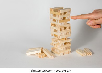 Wooden Board Game On A White Background. People Play A Game Of Chance In Which Balance Is Important. A Tower Of Wooden Blocks And A Human Hand Pulling Out A Piece Per Hour. Free Space For Text