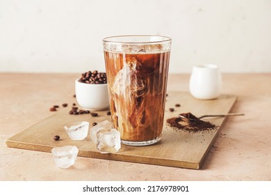 Wooden board with glass of cold brew and coffee beans on beige table