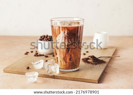 Wooden board with glass of cold brew and coffee beans on beige table