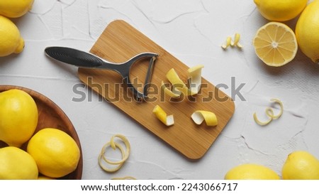 Wooden board, lemons, peeler and fresh rind on white textured table, flat lay