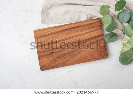 Wooden board with napkin and plant on marble kitchen table, top view