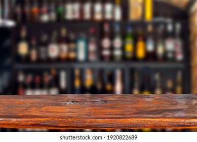 Wooden board on a background of bottles with alcohol. Old bar counter as layout for design. Workpiece for design. Empty place to advertise products. Blurred interior of the bar in the background. - Shutterstock ID 1920822689