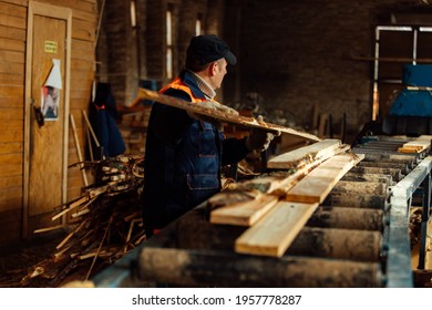 Wooden Board On The Conveyor. People Work On An Automated Sawmill. Industrial Enterprise For Wood Processing. A Worker Carries A Board For Sawing