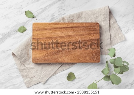 Wooden board on linen napkin on marble kitchen table withgreen leaf, flatlay