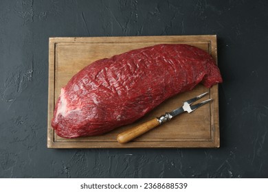 Wooden board with piece of raw meat and fork on black table, top view - Shutterstock ID 2368688539