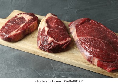 Wooden board with pieces of raw beef meat on grey table - Shutterstock ID 2368688497