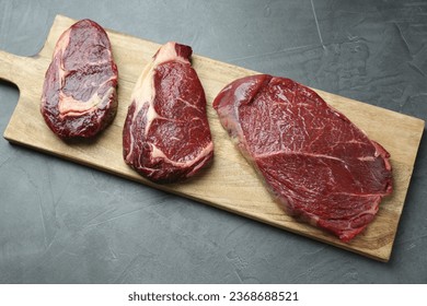 Wooden board with pieces of raw beef meat on grey table - Shutterstock ID 2368688521