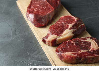Wooden board with pieces of raw beef meat on grey table - Shutterstock ID 2368688543