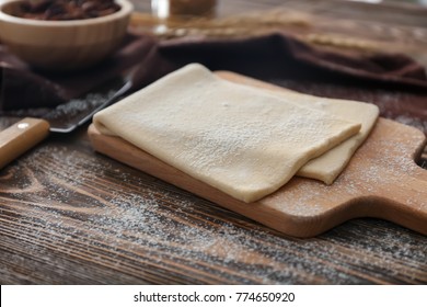 Wooden board with raw flaky dough on table