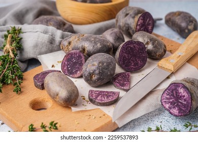 Wooden board with raw purple potatoes and knife on table, closeup - Shutterstock ID 2259537893