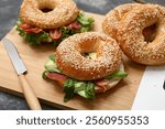 Wooden board of tasty bagel sandwiches with ingredients on black background