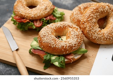 Wooden board of tasty bagel sandwiches with ingredients on black background