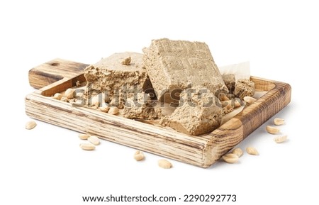 Wooden board with tasty halva and peanuts on white background