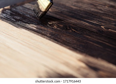 Wooden boards are half covered with stain. A brush with a wooden handle and natural bristles on a background of painted wooden planks. The painting process, the layout.