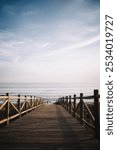 A wooden boardwalk extends toward the sea, illuminated by the warm sunset glow. The calm waters and pastel skies create a peaceful coastal scene