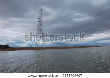 Wooden boardwalk going over the marshes of south San Francisco bay area; electricity towers and lines visible against the cloudy sky; Palo Alto Baylands Park, California