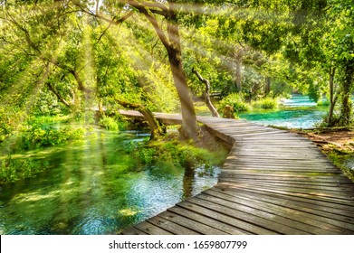 Wooden Boardwalk In The Green Forest Of Krka National Park, Croatia. Beautiful Walking Trail Or Footpath Over The River Near Krka Waterfalls. Scene With Trees And Water On A Sunny Day With Sunrays.