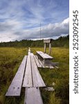 Wooden boardwalk leading through Soisalmensuo swamp in Hollola, Finland, under cloudy sky