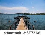 wooden boat dock with a metal hand rail over the rippling blue waters of Lake Allatoona with red buoys and lush green trees, grass and plants with blue sky and clouds at Victoria Beach in Acworth	