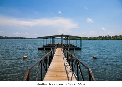 wooden boat dock with a metal hand rail over the rippling blue waters of Lake Allatoona with red buoys and lush green trees, grass and plants with blue sky and clouds at Victoria Beach in Acworth	 - Powered by Shutterstock