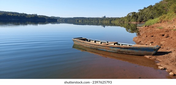 A wooden boat moored by the river. Water mirror reflecting an old boat. Shore of land and stones on the bank of a river - Powered by Shutterstock