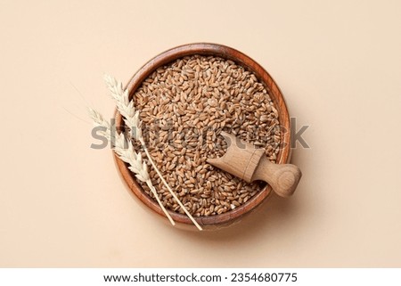 Wooden bowl with grains, wheat ears and scoop on beige background