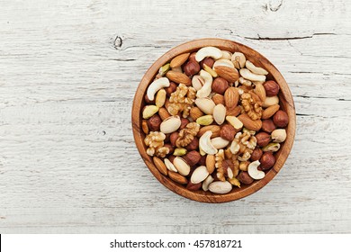 Wooden bowl with mixed nuts on white table from above. Healthy food and snack. Walnut, pistachios, almonds, hazelnuts and cashews. - Shutterstock ID 457818721
