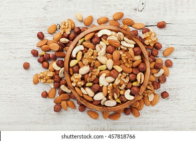 Wooden bowl with mixed nuts on white table top view. Healthy food and snack. Walnut, pistachios, almonds, hazelnuts and cashews. - Shutterstock ID 457818766