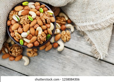 Wooden bowl with nuts on a wooden background, near a bag from burlap. Healthy food and snack, organic vegetarian food. Walnut, pistachios, almonds, hazelnuts and nuts of cashew, walnut. Top view. Vert