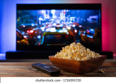 A wooden bowl of popcorn and remote control in the background the TV works. Evening cozy watching a movie or TV series at home - Shutterstock ID 1724395720
