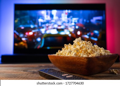 A wooden bowl of popcorn and remote control in the background the TV works. Evening cozy watching a movie or TV series at home