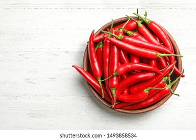 Wooden Bowl With Red Hot Chili Peppers On White Table, Top View. Space For Text