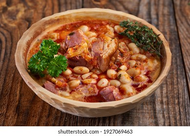 Wooden bowl and spoon with smoked pork leg and beans stew on a rustic table