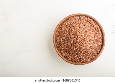 Wooden bowl with unpolished brown rice on a white wooden background. Top view, flat lay, copy space.
