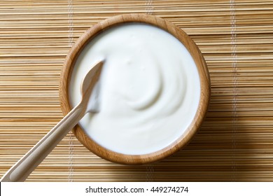 Wooden Bowl Of White Yogurt With Wooden Spoon Inside On Bamboo Matt From Above .