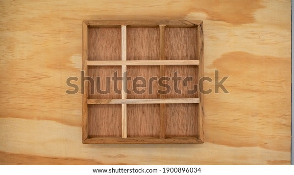 A wooden box with\
empty compartments, suitable for creating a concept or a board game\
of noughts and crosses