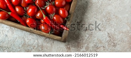 wooden box with fresh cherry tomatoes and chili peppers on the table, space for text