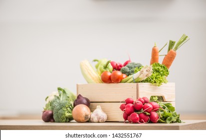 Wooden box full of fresh healthy vegetables. Broccoli carrot radish onion garlic corn on wooden kitchen table.
