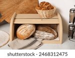 Wooden bread basket, freshly baked loaves and croissants on white marble table in kitchen