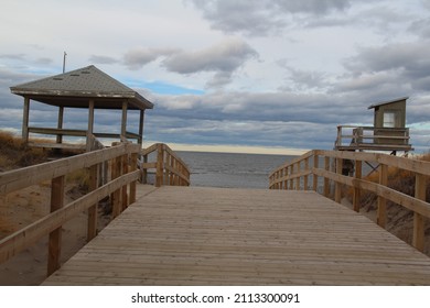 Wooden Bridge By The Sea, With Alittle Pavilion And A Small Tower. There Is A Little Yellowed Grass On The Side. In Front Of The View We Can See The Atlantic Ocean. Parlee Beach, Shediac,New Brunswick