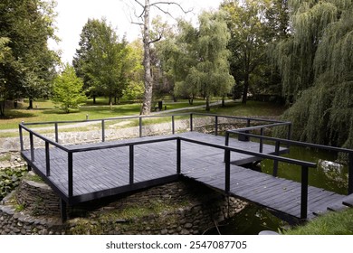 A wooden bridge crossing over a serene lake, surrounded by nature in a peaceful park setting. - Powered by Shutterstock