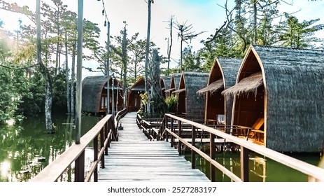 A wooden bridge over a body of water with a row of small wooden cabins on the other side - Powered by Shutterstock