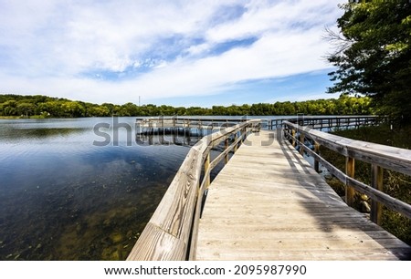 A wooden bridge over the reflective clean lake Carver surrounded by dense trees in Minnesota