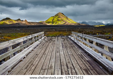 Wooden bridge over a river in ICELAND. Beautiful Icelandic landscape with mountains, sky and clouds. Trekking in national park Landmannalaugar
