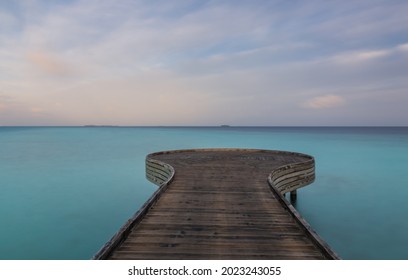 Wooden bridge or pier on tropical white sand beach with clear blue ocean and sky on sunny day. Boardwalk into the ocean and turquoise water. Summer holidays background with copy space. Crossroads