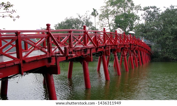 Wooden bridge, wooden pillar supporting the bridge,\
legs spread out, pinning itself into the lake bed, handrails also\
have crossed letters, divided into small cells like the general of\
the chess board